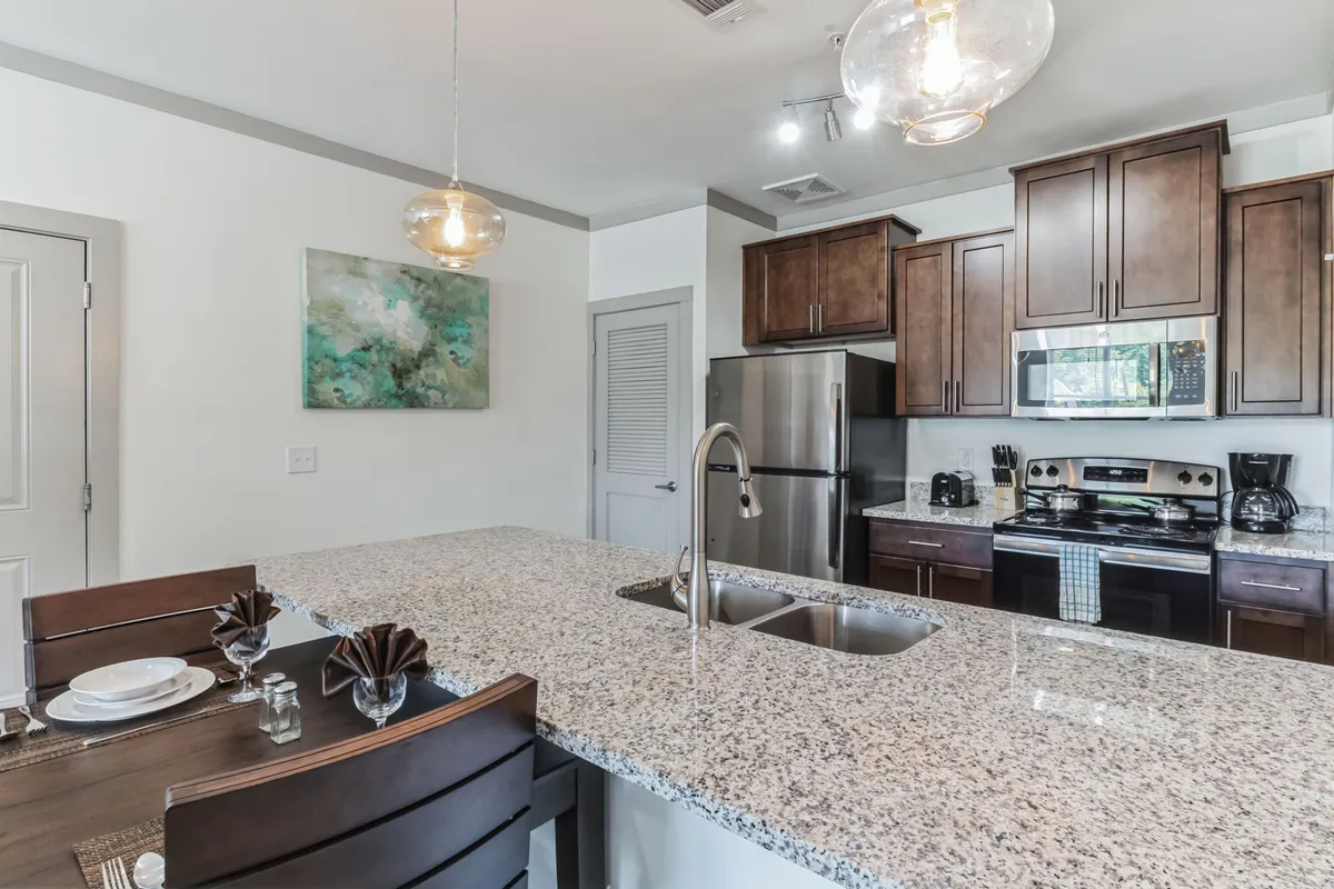 A spacious, light-filled kitchen and dining area with a granite countertop and wooden dining table, complemented by modern kitchen appliances and vibrant artwork on the wall. The scene suggests a welcoming, communal atmosphere ideal for gathering after a day spent exploring the city.