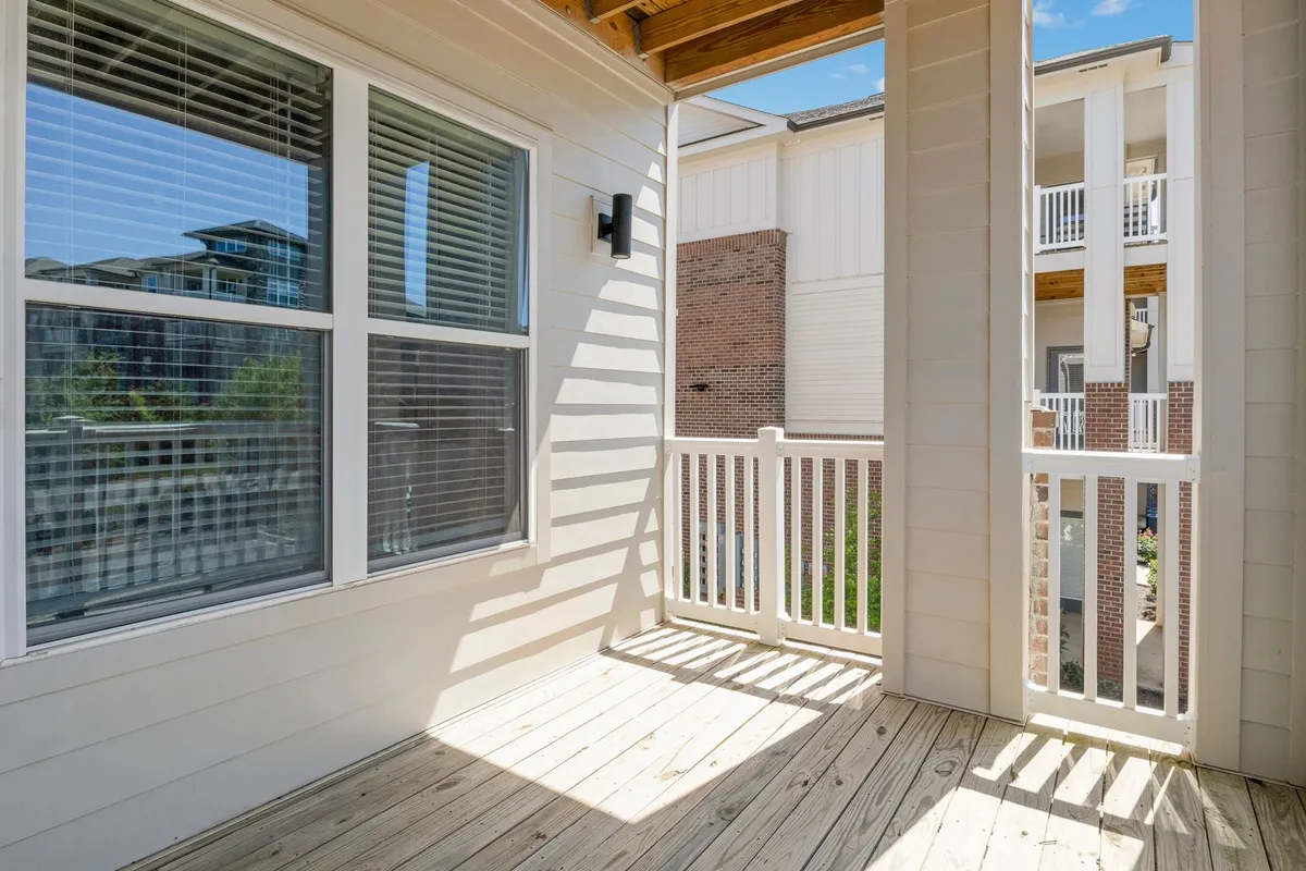 A calm, light-filled room with expansive windows looking out onto a wooden deck framed by crisp white railings. The natural light streams in, illuminating the interior and offering a tranquil setting for relaxation or socializing.