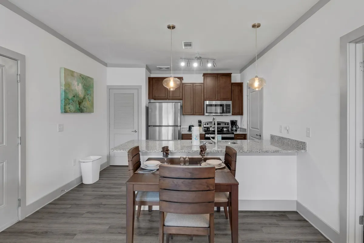 This inviting scene features a dining table elegantly set for a meal, warm pendant lights above, and a backdrop of a modern kitchen complete with stainless steel appliances. The ambiance underscores the potential for both intimate and festive dining experiences.