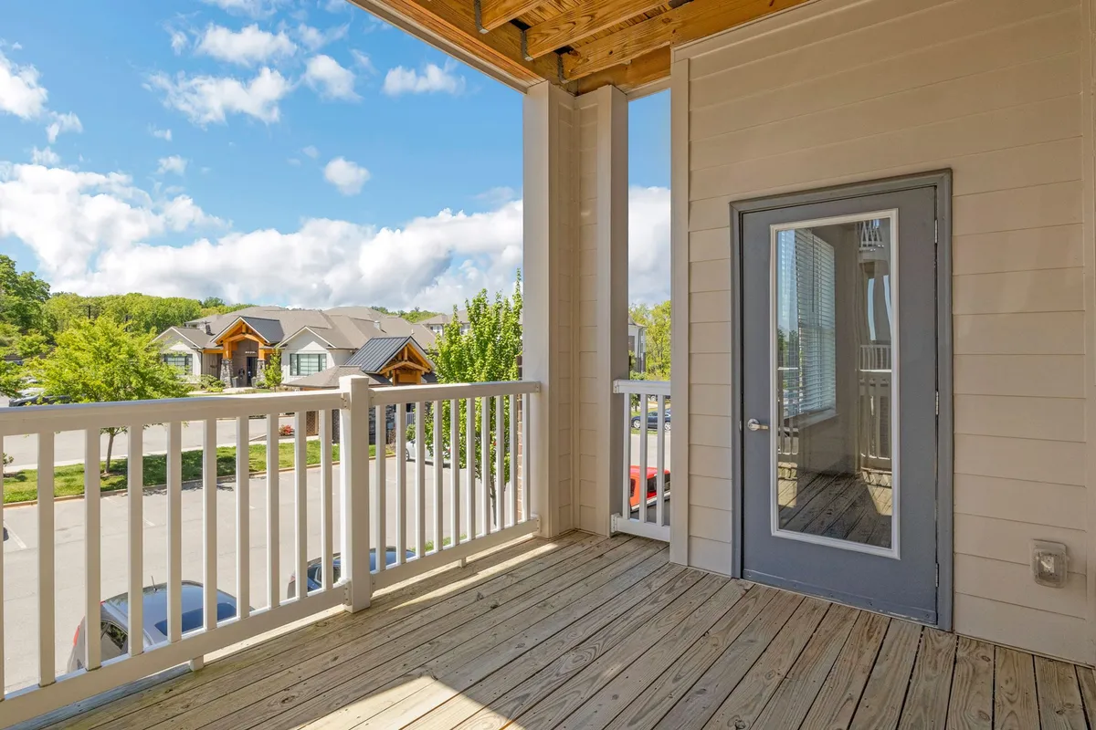 This exterior image features a balcony with a railing overlooking the neighborhood, with the apartment entrance visible. The scene evokes the feeling of enjoying a quiet morning coffee or evening drinks outside, surrounded by the sights and sounds of city life.