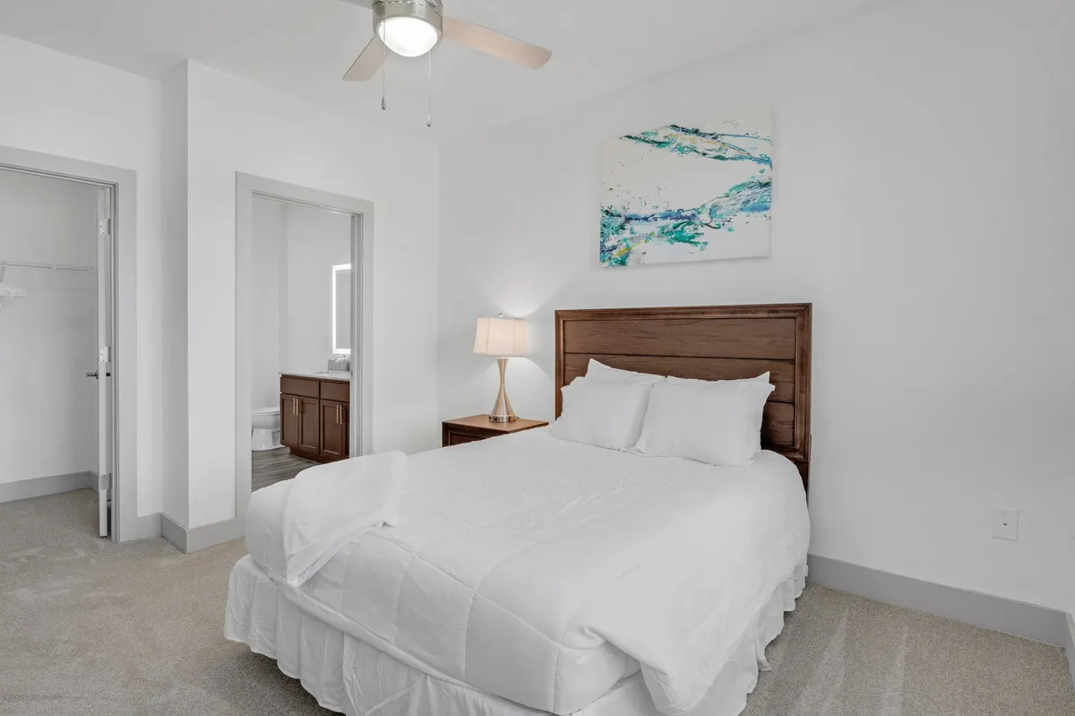 A tranquil bedroom featuring a plush bed with soft, luxe linens, warm ambient lighting from a bedside lamp, and tasteful artwork above the headboard. The mood is serene, inviting relaxation and restful sleep in a private, residential setting.