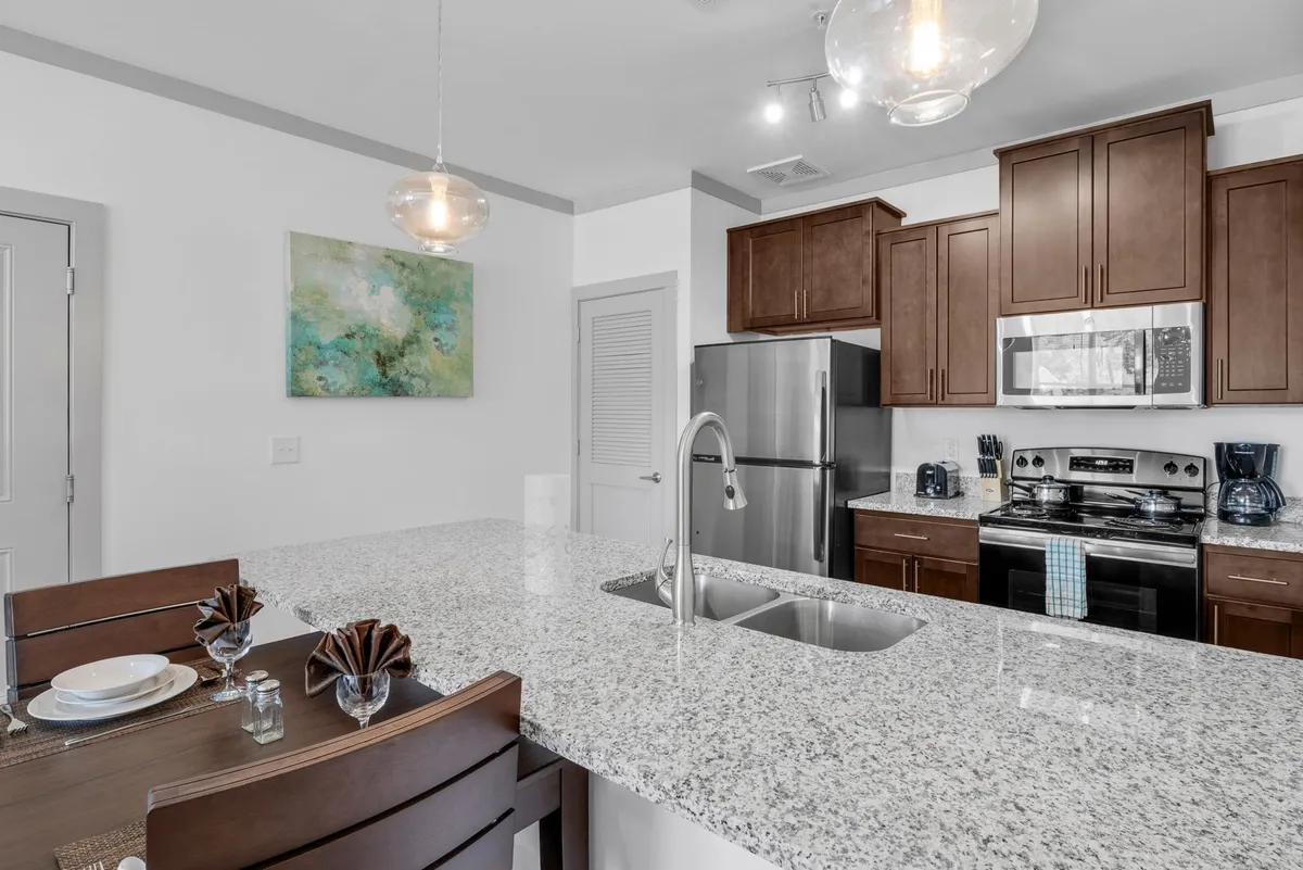 This image showcases an inviting kitchen and dining area, featuring a granite countertop, stainless steel appliances, contemporary artwork, and a well-set dining table. The space seamlessly blends modern amenities with a welcoming atmosphere, capturing both the kitchen workspace and the adjacent dining nook.