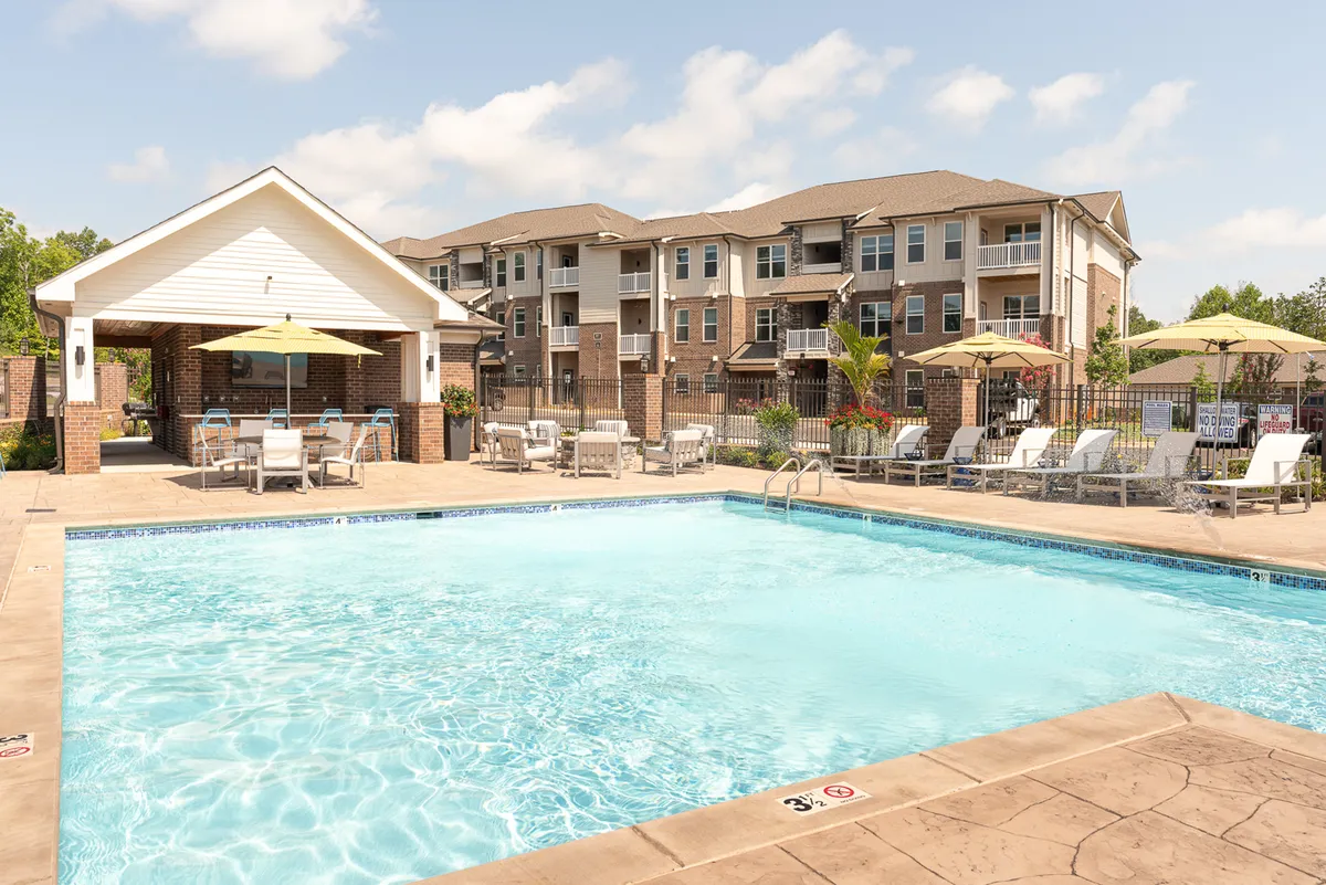 This image features a vibrant outdoor community pool area with ample seating, cabanas, and umbrellas. The surrounding apartment buildings and landscaped grounds offer a glimpse into the community’s social and recreational opportunities, inviting residents to relax or socialize after work.