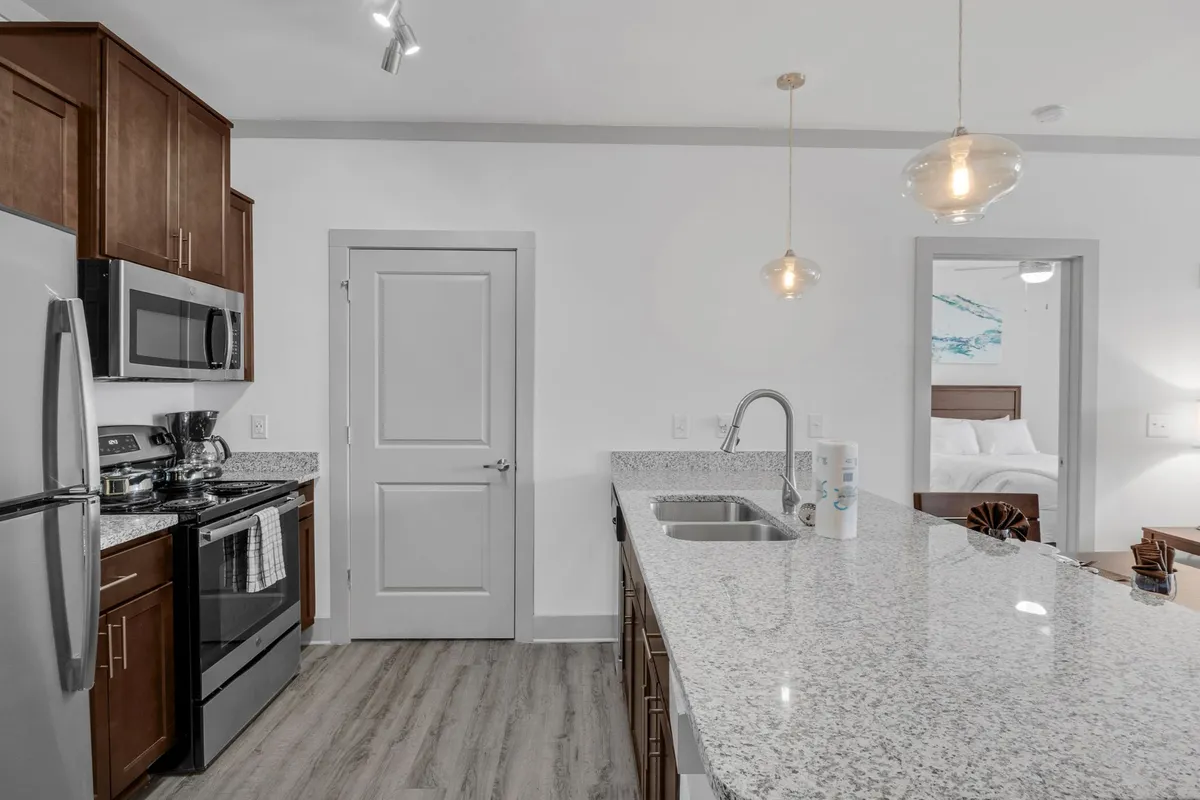 The image highlights a modern kitchen setting with a sleek granite countertop, stainless steel appliances, and stylish pendant lighting above a breakfast bar. The layout invites both culinary creativity and casual dining, emphasizing functionality and design.